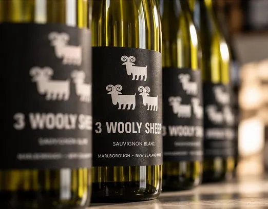 A row of 3 Wooly Sheep bottles faced label-out on a shelf, the black labels reading as one band.