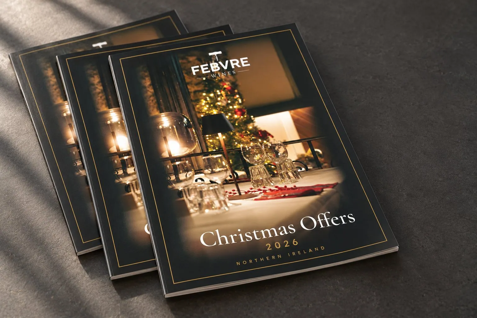 Three copies of the Febvre Christmas Offers 2026 catalogue: a dark cover with a gold keyline framing a candlelit dining table.