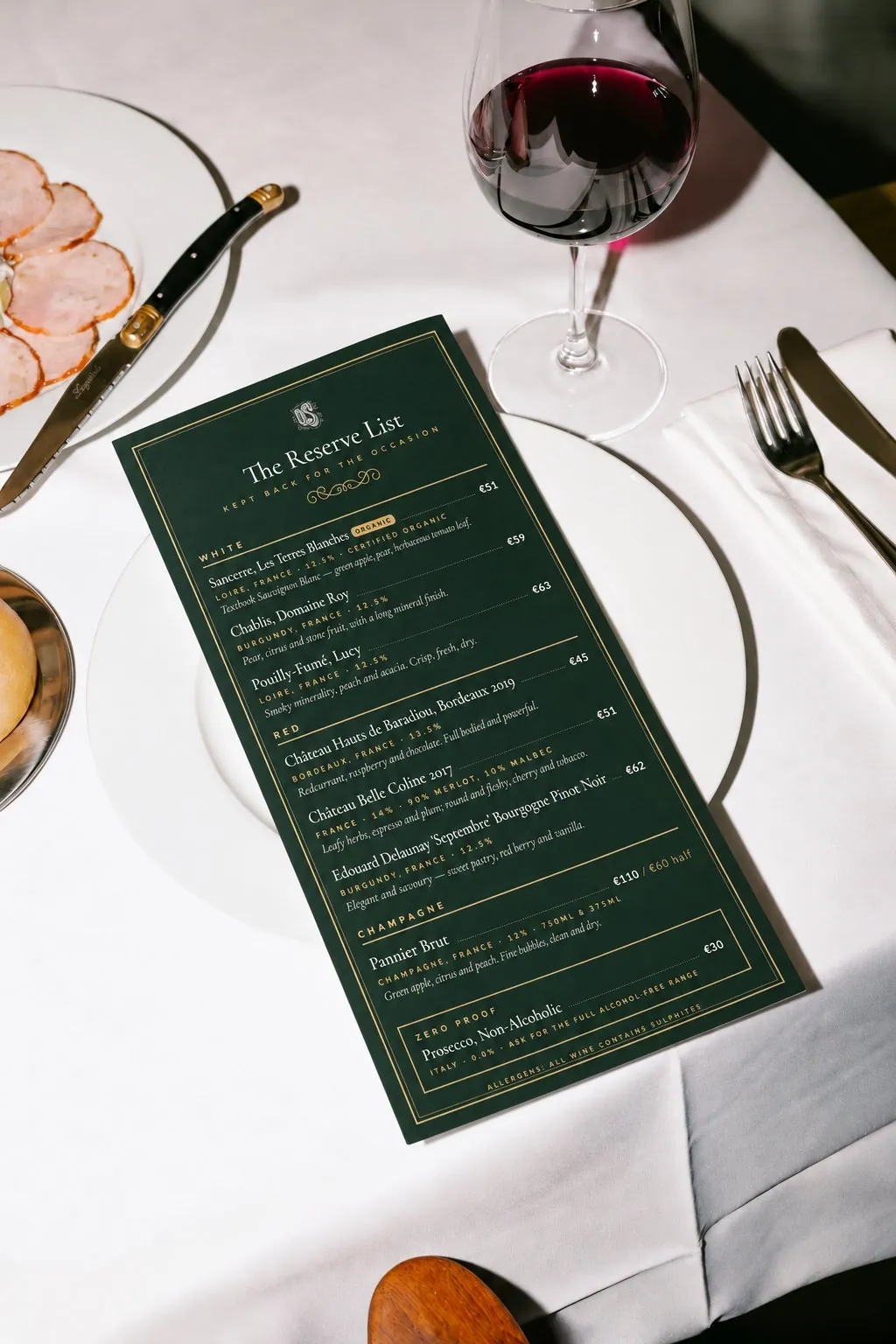 The dark green Reserve List card on a plate beside a glass of red wine