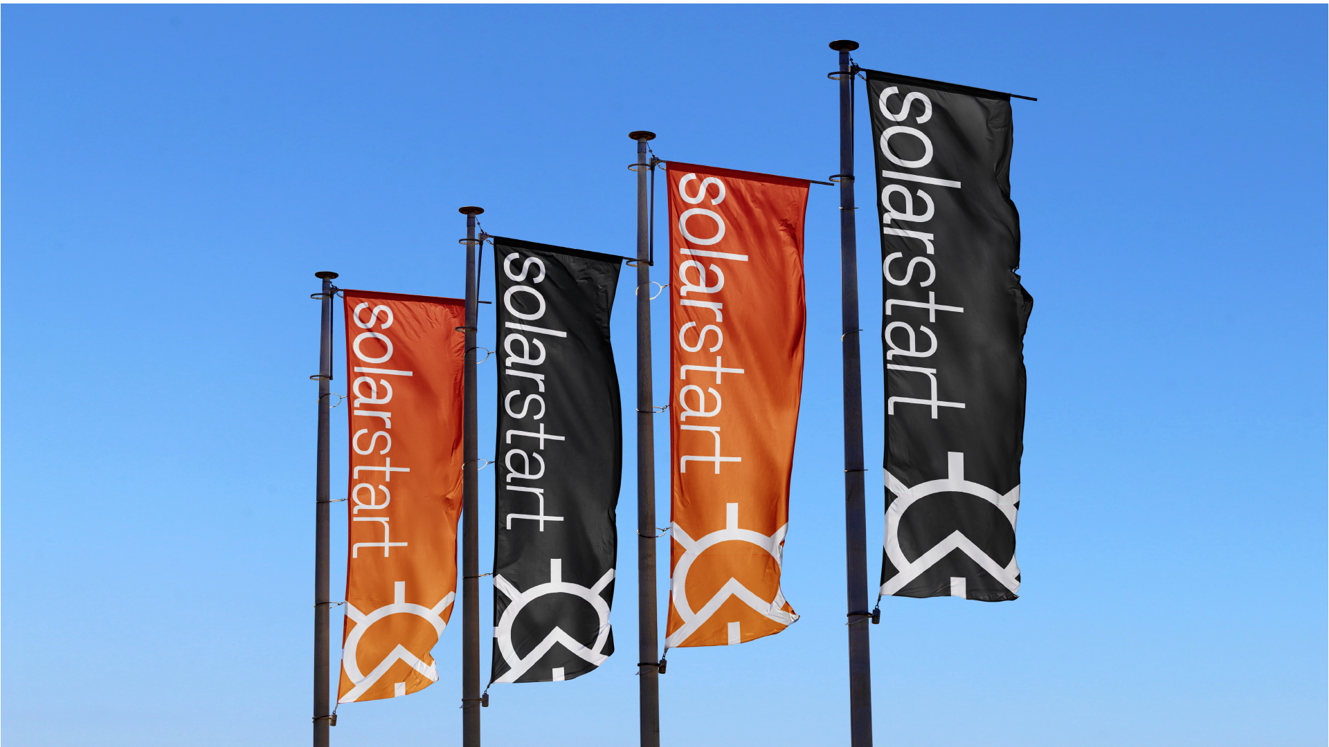 Four flags against a blue sky, alternating orange and black, each carrying the solarstart wordmark and mark