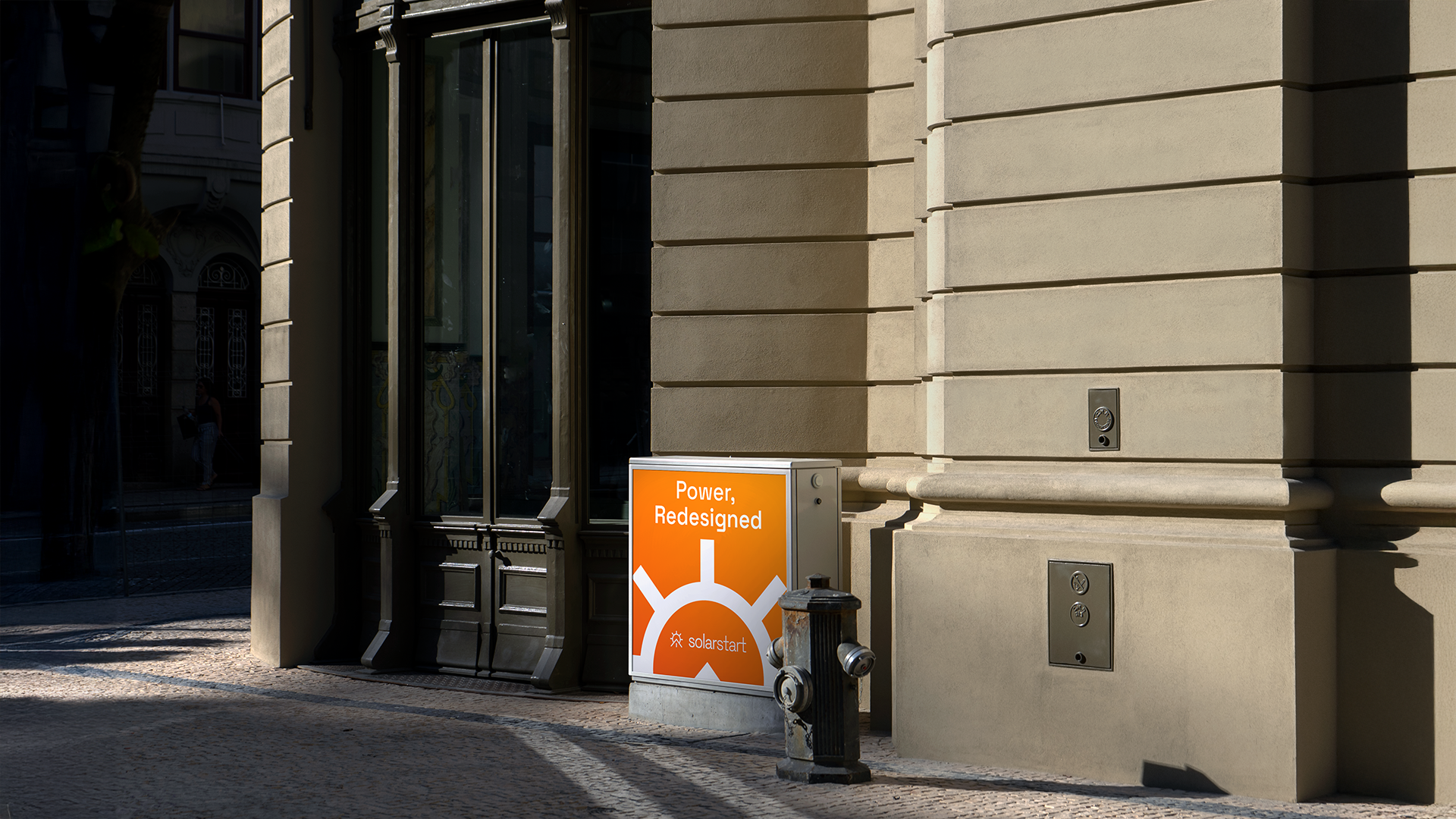 A street utility box wrapped in an orange gradient panel reading 'Power, Redesigned' with the solarstart mark, set against a stone building facade