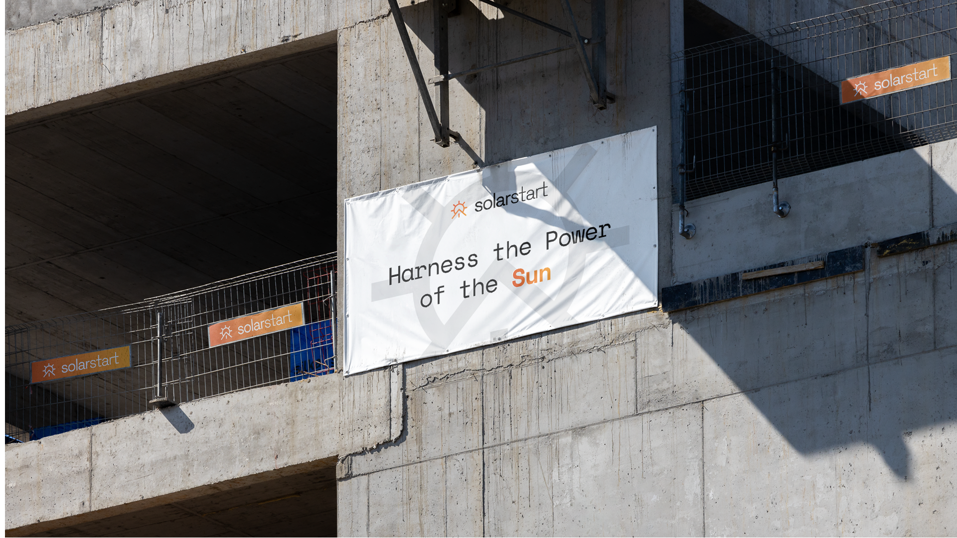 A construction-site banner reading 'Harness the Power of the Sun' mounted on a concrete building under construction, with smaller solarstart tags visible on scaffolding netting nearby